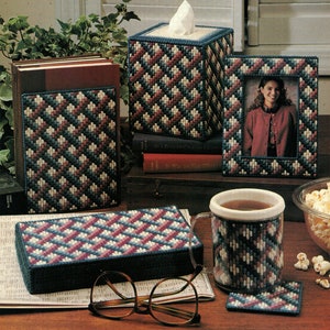 May include: A set of four plastic canvas craft projects featuring a geometric pattern in shades of blue, pink, and white. The projects include a tissue box cover, a picture frame, a mug cozy, and a coaster.