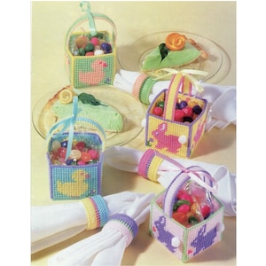 Puede incluir: Cuatro cestas de Pascua coloridas llenas de caramelos de goma. Cada cesta tiene un diseño diferente, incluyendo un pato, un conejito y una flor. Las cestas están hechas de lona de plástico y son perfectas para guardar pequeños regalos o golosinas.