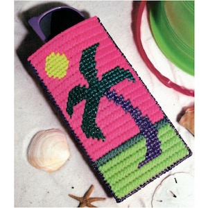 May include: A pink, green, and purple plastic canvas sunglasses case with a palm tree and sun design.