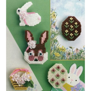 May include: Five plastic canvas Easter crafts: a white bunny, a brown bunny, a basket with pink flowers, a brown egg with yellow flowers, and a white egg with pink flowers.