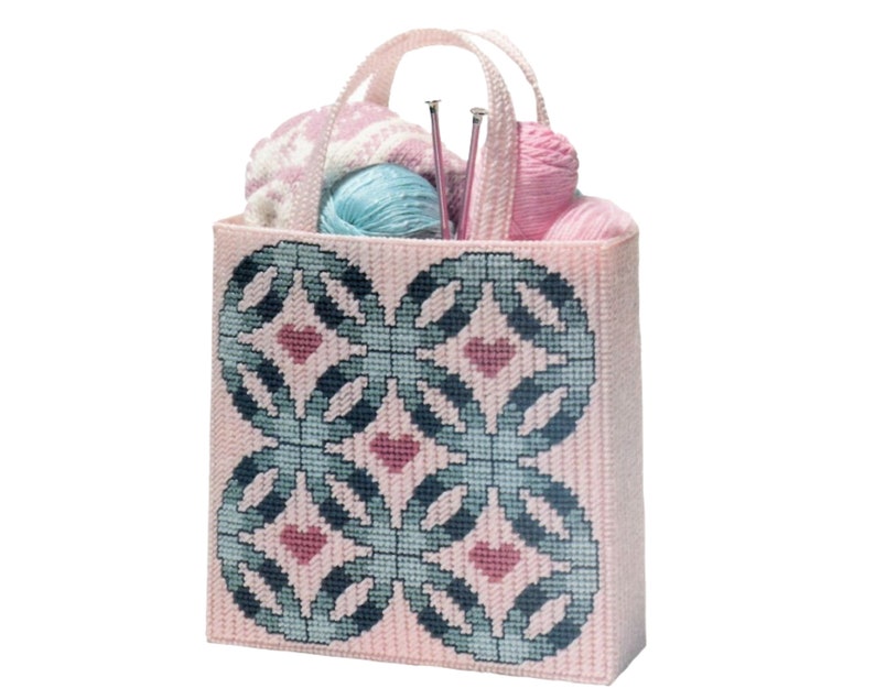 May include: A pink needlepoint tote bag with a geometric design in teal and pink, filled with yarn and knitting needles. The bag has a matching handle and is filled with pink, blue, and white yarn balls.