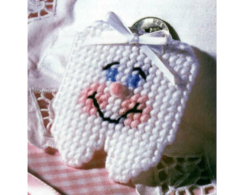 May include: A white crocheted tooth with a pink and blue smiling face. The tooth has a white ribbon tied around it.