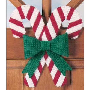 Op de afbeelding: Een kerstkrans gemaakt van twee snoepstokken met rode en witte strepen, gebonden met een grote groene strik.