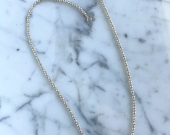 May include: A delicate gold and silver beaded necklace with a simple clasp closure. The necklace is made of small, round beads that are evenly spaced.