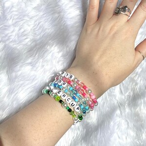 Op de afbeelding: Een stapel kleurrijke kralenarmbanden met witte letterkralen die "BIG" en "SUPER CUP" spellen.