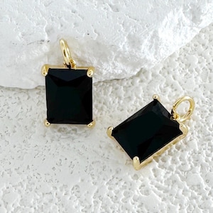 Peut inclure: Deux breloques dorées avec des pierres précieuses carrées noires. Les breloques ont une boucle en haut pour les attacher à un collier ou un bracelet.