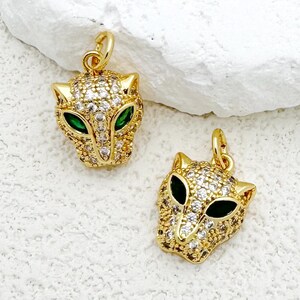 Può includere: Due ciondoli pendenti a forma di testa di pantera, color oro. I ciondoli sono incrostati di strass trasparenti e hanno occhi in smalto verde.