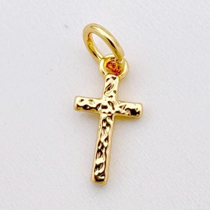 Puede incluir: Un pequeño dije de cruz de oro con una superficie texturizada. El dije tiene un bucle en la parte superior para sujetarlo a un collar o pulsera.