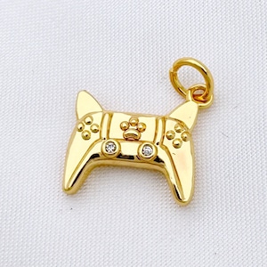 May include: A gold-tone pendant charm shaped like a video game controller with small clear rhinestones. The charm has a loop at the top for attaching to a necklace or bracelet.