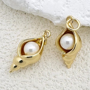 May include: Two gold-tone shell charms with a white pearl inside. The charms are perfect for adding a touch of elegance to jewelry projects.
