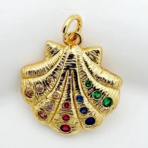 May include: A gold-colored seashell pendant with a loop for a chain. The pendant is adorned with colorful gemstones, including red, blue, green, and clear stones. The seashell design has detailed ridges.