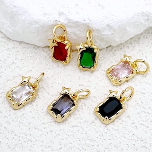 Puede incluir: Seis abalorios de tono dorado con piedras de cristal de diferentes colores. Cada abalorio tiene dos pequeños acentos en forma de estrella. Los abalorios están sobre una superficie blanca.