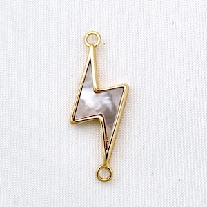 Op de afbeelding: Goudkleurige bliksemhanger met een witte parelmoer inleg. De hanger heeft twee springringen om aan sieraden te bevestigen.