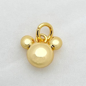 以下が含まれることがあります： ミッキーマウスの頭の形をした金色のチャーム。チャームは、大きな中央の球体と、両側に2つの小さな球体、上部にアタッチメント用のループを備えています。チャームは非常に反射性があります。