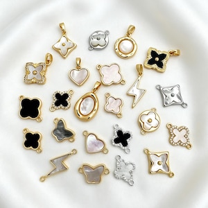 Puede incluir: Una colección de dijes de metal en tonos oro y plata con diversas formas, incluyendo tréboles de cuatro hojas, corazones, mariposas y rayos, con incrustaciones de nácar blanco, negro y gris, y detalles de cristales transparentes.