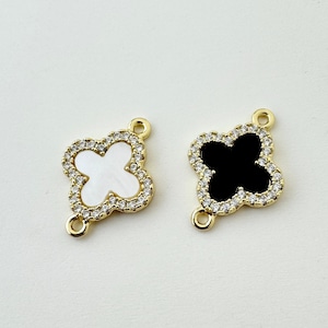 May include: Two clover-shaped charms. One charm features a white center, the other a black center. Both are outlined with clear crystals and have gold-colored loops for attachment, ideal for jewelry making.