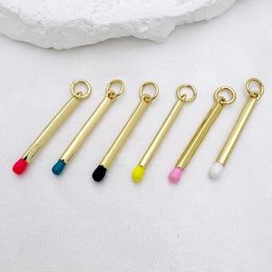 Può includere: Sei ciondoli a forma di fiammifero color oro con punte colorate. Le punte sono rosse, verde acqua, nere, gialle, rosa e bianche. Ogni ciondolo ha un piccolo anello nella parte superiore per il fissaggio.