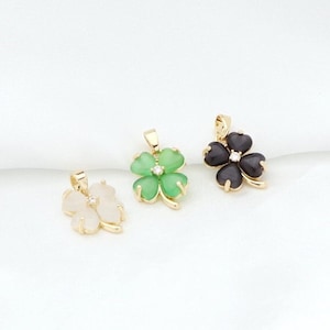 May include: Three gold four-leaf clover pendants with different colored stones. The pendants are on a white background. The stones are green, white, and black.