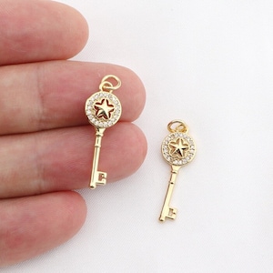 May include: Two gold key charms with a star-shaped design in the center of the keyhole. The star is surrounded by clear rhinestones.