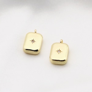 May include: Two gold-tone pendant charms with a single clear rhinestone in the center of each. The charms are square shaped with rounded corners.
