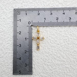 May include: A gold-tone cross pendant with clear cubic zirconia stones. The pendant is approximately 1.5 inches tall and is measured against a ruler.
