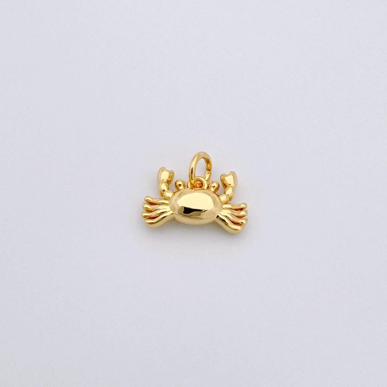 May include: A gold-colored crab charm pendant. The charm is detailed with small claws and a rounded body.