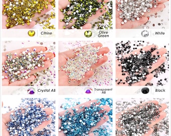 Könnte beinhalten: Sortiment an runden, flachen Strasssteinen in verschiedenen Farben, darunter Citrin, Olivgrün, Weiß, Kristall AB, Transparent AB, Schwarz, Hellblau, Aquamarin und Grau.