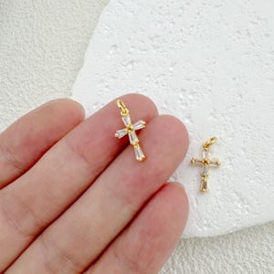 May include: Two gold cross charms with clear crystal accents. The charms are small and delicate, perfect for adding a touch of sparkle to jewelry.