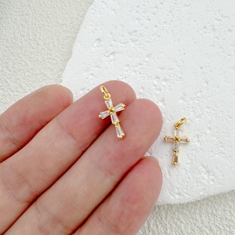 May include: Two gold cross charms with clear crystal accents. The charms are small and delicate, perfect for adding a touch of sparkle to jewelry.