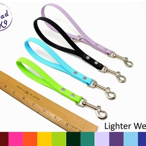 May include: Three dog leashes in different colors: lavender, turquoise, and lime green. Each leash has a silver clip and silver dots. The leashes are laid out on a white surface with a wooden ruler and a color swatch card below. The text "Lighter Weight" is visible below the leashes.