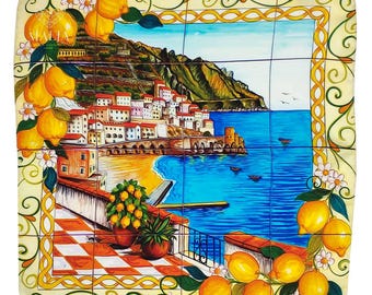 May include: A square ceramic tile mural depicting a coastal Italian town scene. The artwork features a vibrant blue sea, a sandy beach, and buildings with red-tiled roofs. Yellow lemons and white flowers adorn the border, creating a sunny, Mediterranean feel.