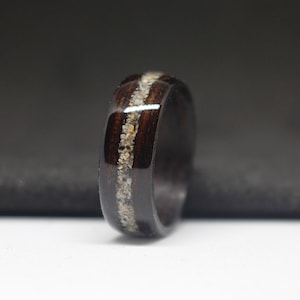 May include: A dark brown wooden ring with a thin band of white inlay. The ring is smooth and polished.