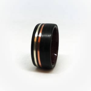 May include: A black wooden ring with silver and copper metal inlays. The ring has a dark red interior. The ring is a close-up shot against a white background.