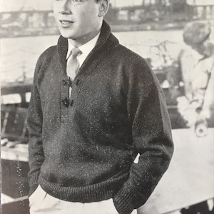 May include: A black knitted sweater with a high collar and a button closure. The sweater has a textured knit pattern and is worn by a man in a black and white photo.