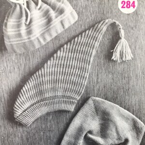 以下が含まれることがあります： 縞模様のニット帽と、タッセル付きのニット帽が2つ、合計3つのニット帽。ニット帽は、質感のある表面の上に置かれています。画像には、284という数字が印刷されています。