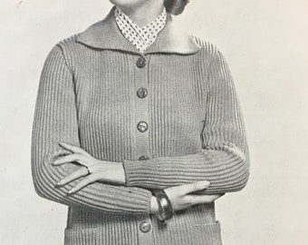 May include: A close-up of a woman wearing a gray knitted cardigan with a collared neckline and button closure. The cardigan has two pockets on the front and is ribbed throughout. The woman is wearing a white blouse with a small pattern underneath the cardigan.