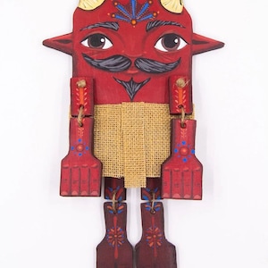 May include: A red wooden folk art figure with a devil-like face, featuring horns, a mustache, and decorative patterns. The figure has jointed arms and legs, with a burlap midsection. The artwork is painted with vibrant colors and intricate details.
