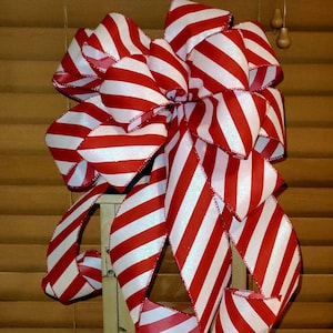 May include: A large red and white striped bow with a glittery finish. The bow is tied around a wooden lantern.