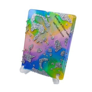 Pode incluir: Um caderno espiral colorido com um design de arco-íris e glitter prateado. A capa tem o texto "Kaektage in Glitzer tunken und funkeln lassen".