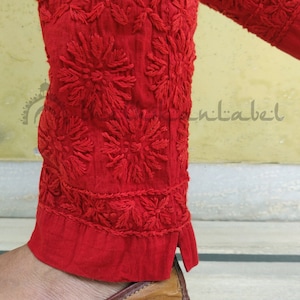 May include: Red cotton pants with intricate embroidered floral designs. The pants have a wide leg and a flared bottom. The embroidery is done in a traditional style and is very detailed. The pants are worn with brown leather flats.