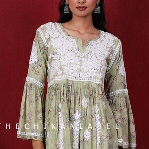 May include: A green and white floral print kurta with white embroidery and bell sleeves. The kurta is paired with matching pants. The model is wearing silver earrings.
