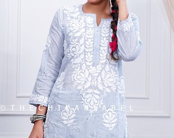 Puede incluir: Una kurta de algodón azul claro con bordados blancos con motivos florales. La kurta se combina con pantalones palazzo a juego. La modelo lleva sandalias doradas.