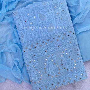 May include: A light blue embroidered fabric with silver sequins and mirror work. The fabric is folded in half and has a sheer light blue fabric underneath. The text "@thechikanlabel" is visible in the image.
