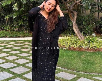 May include: A black long-sleeved dress with a sparkly design. The dress is worn by a person standing on a stone path with green grass.