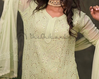 May include: A light green embroidered kurta with a V-neckline and a matching dupatta. The kurta is decorated with intricate mirror work and has a delicate lace trim. The dupatta is sheer and has a floral design.