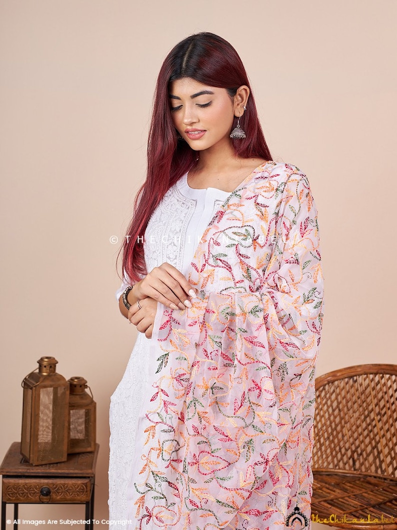 Pu&ograve; includere: Una dupatta bianca ricamata con un motivo floreale in tonalit&agrave; di rosa, rosso, verde e giallo. La dupatta &egrave; realizzata in un tessuto trasparente e ha un aspetto delicato e femminile.