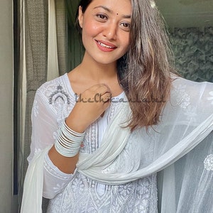 May include: A woman wearing a white embroidered kurta with a white dupatta draped over her shoulders. She is wearing silver bangles on her wrist. The text "thechikanlabel" is visible in the image.