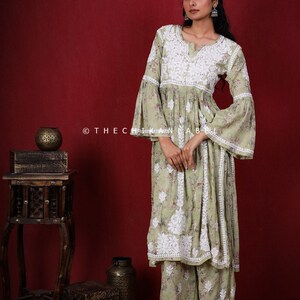 May include: A light green, long-sleeved, embroidered kurta with a white floral pattern. The kurta has a bell sleeve and a gathered waist. The model is wearing the kurta with matching palazzo pants.