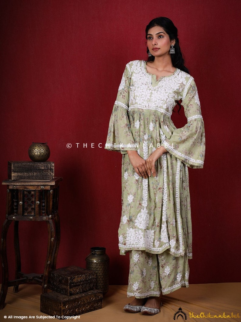 May include: A light green, long-sleeved, embroidered kurta with a white floral pattern. The kurta has a bell sleeve and a gathered waist. The model is wearing the kurta with matching palazzo pants.