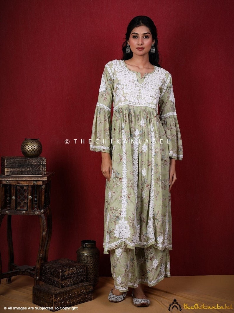 May include: A green and white floral print kurta with white embroidery and bell sleeves. The kurta is paired with matching pants. The model is wearing silver earrings.
